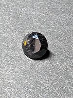 Close-up front angled view of the 6mm black carbonado diamond showing faceted round cut surface on textured gray background.