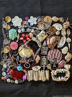 Top view of assorted natural seashell, ammonite and mother of pearl pendants along with bracelets and necklace pieces spread on black fabric background.
