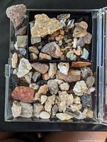 Top down view of box filled with various mineral and rock specimens of differing sizes and colors.