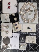 Top down image showing assorted new, carded genuine cultured pearl earrings in various colors and styles, plus a bracelet and necklace set with pearls and crystals.
