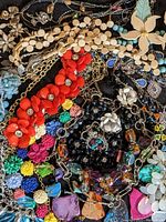 Image showing multiple colorful floral-themed statement necklaces piled together on a dark cloth background.