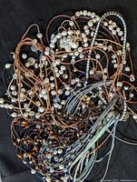 Overhead photo showing multiple freshwater cultured pearl necklaces and bracelets tangled together on a dark background, with pearl sizes ranging from small to medium attached to various colored leather and silk cords.