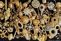 Top-down view of assorted gold-tone costume jewelry brooches featuring faux pearls in various styles and arrangements, some brooches show signs of wear and some pearls missing.