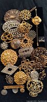 Close-up of mixed large filigree and emblem style costume jewelry brooches in gold and silver tones, various shapes and textures.