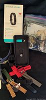 Photo showing new Fitbit Alta in box, Ziploc bag with multiple Fitbits, and phone case with assorted straps below