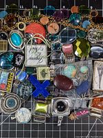 Top view showing a large variety of glass necklace pendants in multiple colors and designs laid out on a black grid surface.