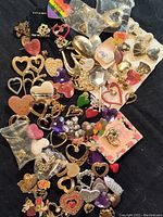 Full assortment of heart-shaped costume jewelry brooches in various materials, colors, and designs spread out on a black background.