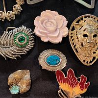 Close-up of six assorted decorative belt buckles featuring metal and plastic materials with detailed designs and colored accents.