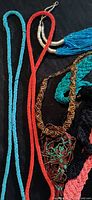 Assorted micro seed bead necklaces laid on black background showing varied styles and colors including turquoise, red, brown, black, pink beads and multi-strand designs.