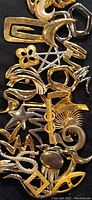 Close up of assorted gold and silver tone abstract modernist motif costume brooches showing various artsy squiggles, scrolls, and geometric shapes on black background.