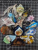 Top view of all 13 assorted Venetian Murano style art glass pendants arranged on black grid mat, showing various colors and shapes.