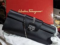 Front view showing black satin clutch atop dust bag with Ferragamo box in background