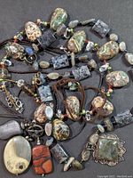 Overview of assorted semi-precious stone necklaces with varied beads and pendants laid out on dark fabric.