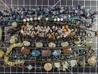 Full lot image showing several strands of stone bead necklaces and bracelets arranged horizontally on a grid background.
