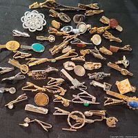 Full view of the collection showing numerous tie clips with varied decorative accents including stones, metalwork, and shapes.
