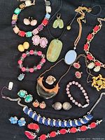 Photo showing an assortment of vintage costume jewelry including colorful thermoset plastic bead necklaces, earrings, bracelets, and brooches placed on black fabric
