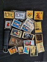 Photo of assortment of USPS stamp-themed pins and one wristwatch missing a strap, showing colorful collectible stamp designs in pin form and the watch face resembling a stamp.