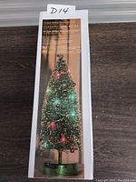 Photo showing the product box with an image of a decorated green glitter Christmas tree approximately 14 inches tall. Box text indicates features include battery powered LED lights and decorations.