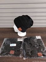 Two black Bluetooth toques, one displayed on a mannequin head and two packaged in clear plastic, shown against a gray corrugated metal background.