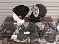 Four Bluetooth toques on display: two black knitted fleece-lined floppy toques and two black fuzzy water-repellent toques with fur-lined ear flaps and face masks. All have leather Bluetooth patches.