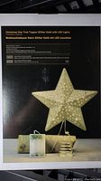 Photo of packaging showing product name and image of gold glitter star tree topper with LED lights and battery pack