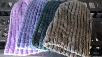 Photo showing four knitted toques laid out side by side in colors purple, blue, green, and grey on a dark surface.