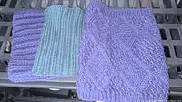 Photo of three knit neck warmers laid side by side on a black surface. The neck warmers are in light purple, light green and purple mix, and light purple patterned knit.