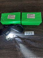 Photo showing 2 green packages, 1 black rechargeable headlamp with attached strap, 1 white USB charging cable, and a lot number card.