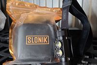 Packaged Slonik headlamp set including the headlamp mounted on the strap, battery, and black hard case sealed within clear plastic bag