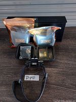 Photo showing all lot contents: Slonik headlamp with black strap, two sealed battery pouches with Slonik label, small black zippered hard case, and black retail box.