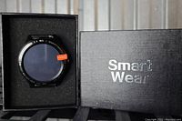 Smart Watch in black box with 'Smart Wear' branding, showing round watch face and black metal band.