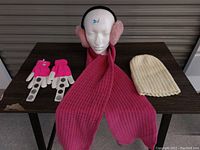 Photo of the full set displayed on a table and mannequin head showing gloves, scarf, knit toque, and pink earmuffs.
