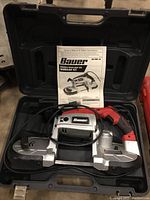 Overall view of Bauer bandsaw kit inside black carrying case with the owner's manual placed inside the case behind the bandsaw.