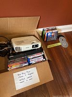 Box containing Samsung Blu-ray player, Epson projector, Blu-ray and DVD movies, and power cords.