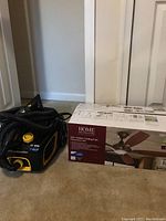 Photo of McCulloch canister vacuum and boxed Home Decorators Collection ceiling fan on carpet against wall.