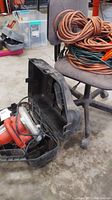 Black & Decker circular saw in open plastic carrying case on floor next to office chair with extension cords coiled on it.