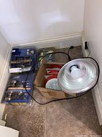 View of the whole lot: two Schlage door knob sets in packaging, other door knob in packaging, box containing wrapped fire alarms, and work light with bulb and cord on tiled floor near baseboard.
