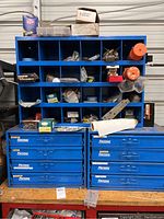 Overall view of three blue storage units (one cubby shelf on top of two drawer units) containing assorted hardware and tool accessories.