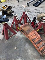 Four large red adjustable jackstands, two smaller red adjustable jackstands, and one orange vehicle ramp arranged on the floor.