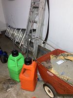 Photo showing Werner multi-position ladder, step ladder leaning against wall, green and orange fuel cans, and red wheelbarrow with Quikrete bags.