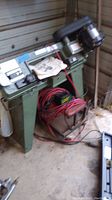 Front view of bandsaw on stand with battery charger and cables on floor