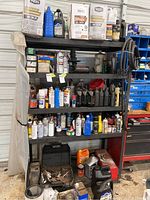Shelf with various automotive fluids including motor oils and spray paints with tins and cans on multiple shelves. Tool chest visible on right side but not included in sale.