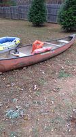 Photo shows Old Town orange canoe on grass next to inflatable Explorer 99 boat and three orange life vests inside the canoe.