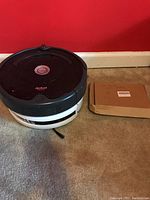 Full view of iRobot Roomba robot vacuum and a cardboard box next to it on carpet.