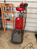 Full view of red steel tank on wheels, black oil pan and manifold gauge set