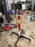 Overall frontal view of red hydraulic transmission jack stand with four-leg caster base.