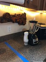 Oster blender with glass pitcher and small white appliance next to it on countertop.