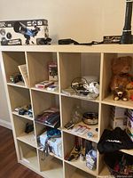 Shelf unit with multiple compartments containing various items including the Maxx Explore telescope box on top, plush toys, electronics, games, tools, and accessories.