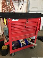 Overall view of red US General Pro roller cart on casters with black top mat and lower shelf holding plastic bin of hardware