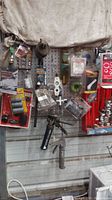 Photo showing jeweler's pegboard with hanging packaged hardware items including light bulbs, hose clamp, battery terminal protectors, and hand tools including a caulk dispenser gun.